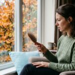 Mujer junto a una ventana en otoño mirando el pelo que ha quedado en su cepillo